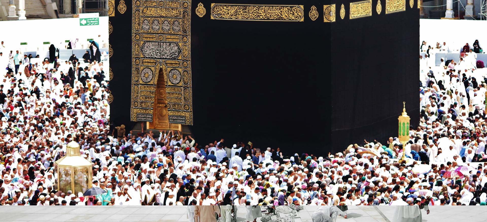 Close-up view of the gold door of the Kaaba with pilgrims pressing against the black cloth and stone base to pray.