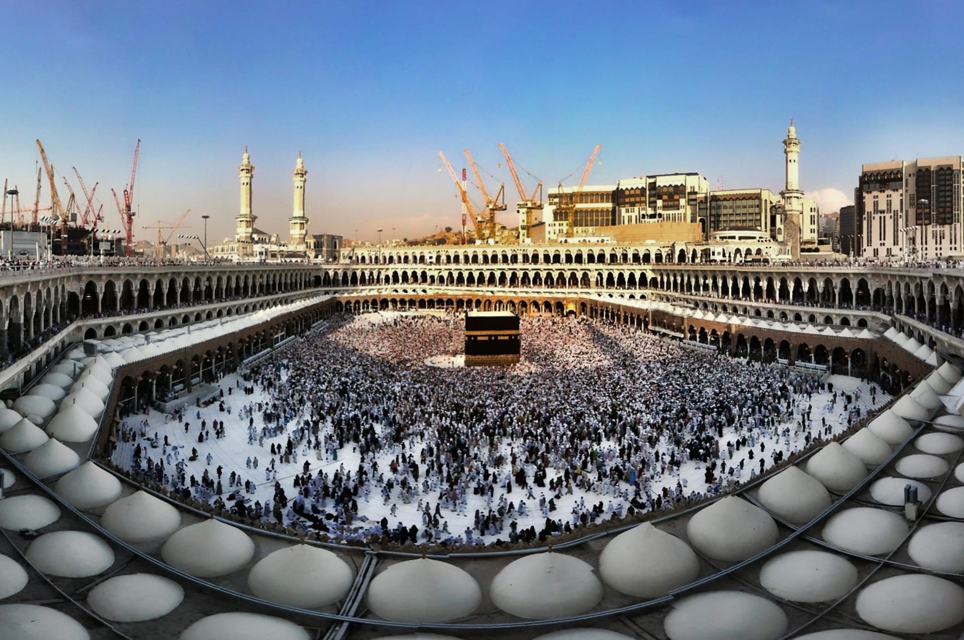 A high-angle view of the Kaaba in the center of the Masjid al-Haram courtyard, surrounded by thousands of pilgrims.