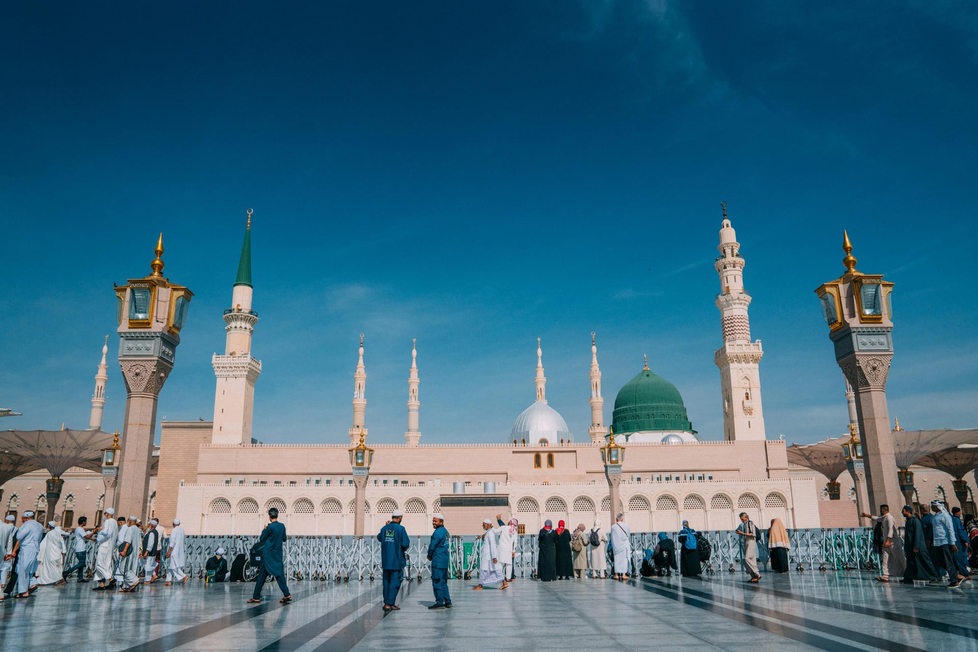 The courtyard of Al-Masjid an-Nabawi in Medina featuring the Green Dome and towering minarets under a clear blue sky.
