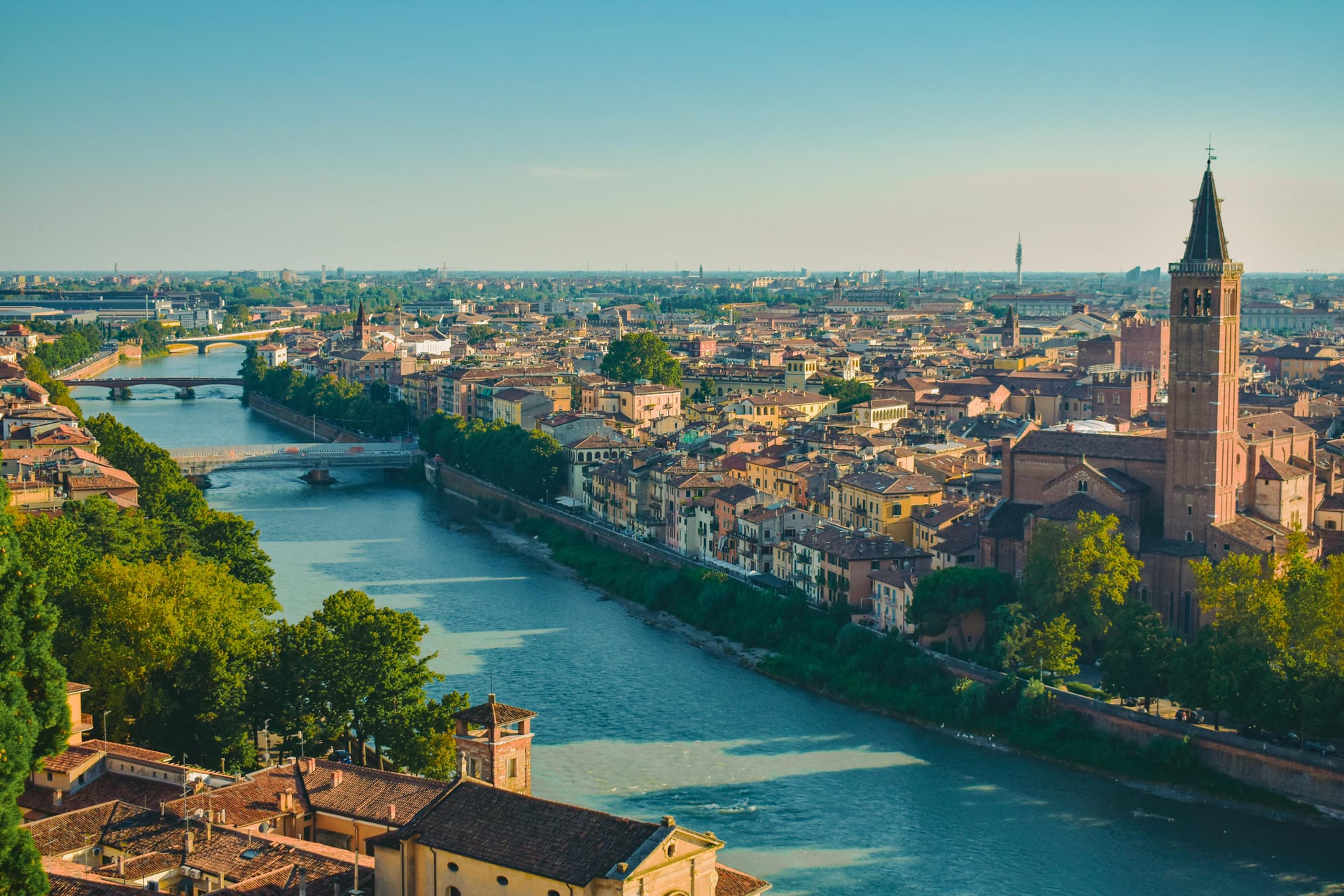 A high-angle view of the Adige River winding through the historic city of Verona, featuring the Ponte Pietra bridge and terracotta rooftops.