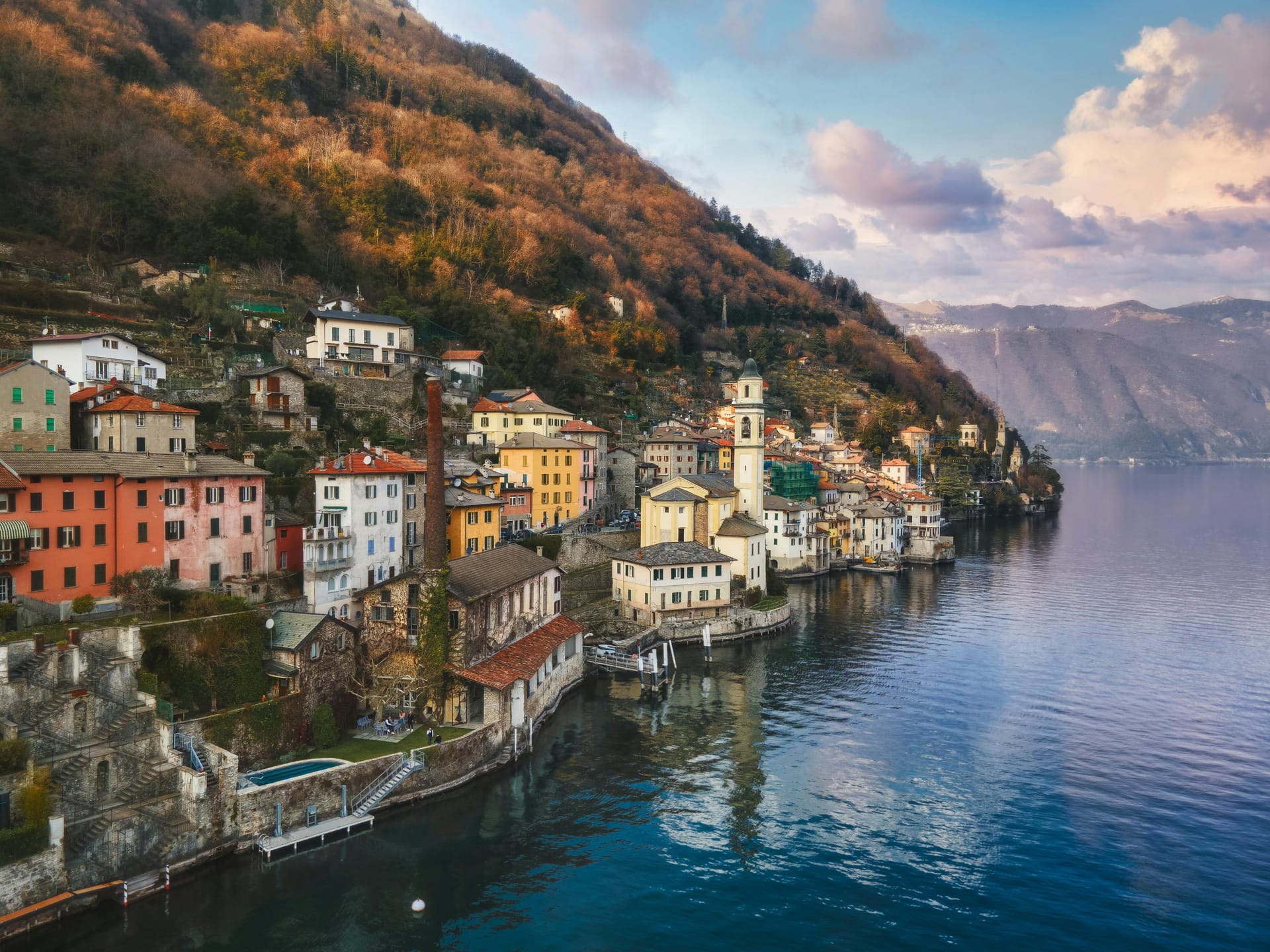 The colorful hillside village of Varenna on the shores of Lake Como, Italy, with a church steeple rising above the buildings near the water.
