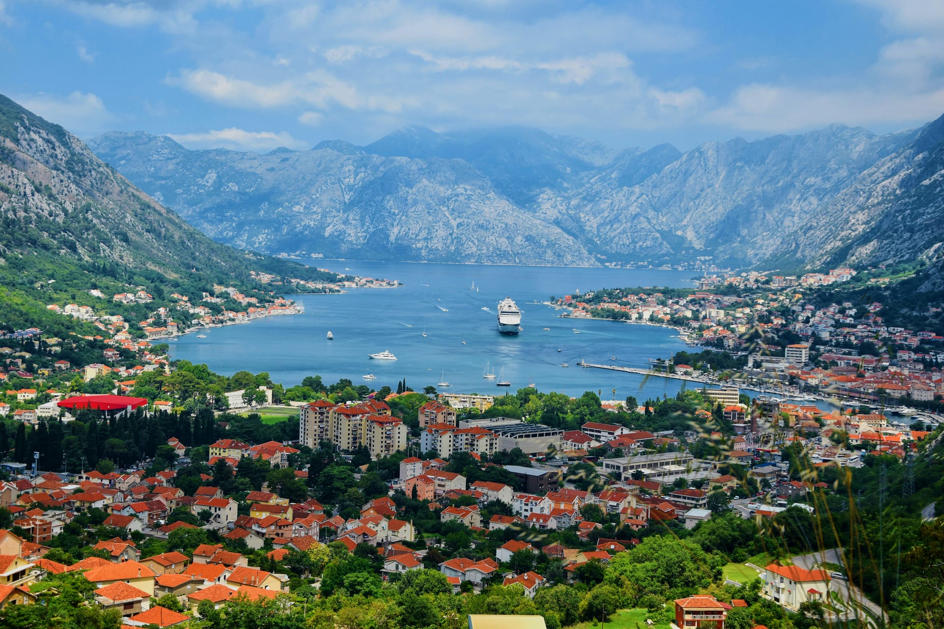 A panoramic view of the Bay of Kotor with steep mountains rising above the coastal towns and blue water.