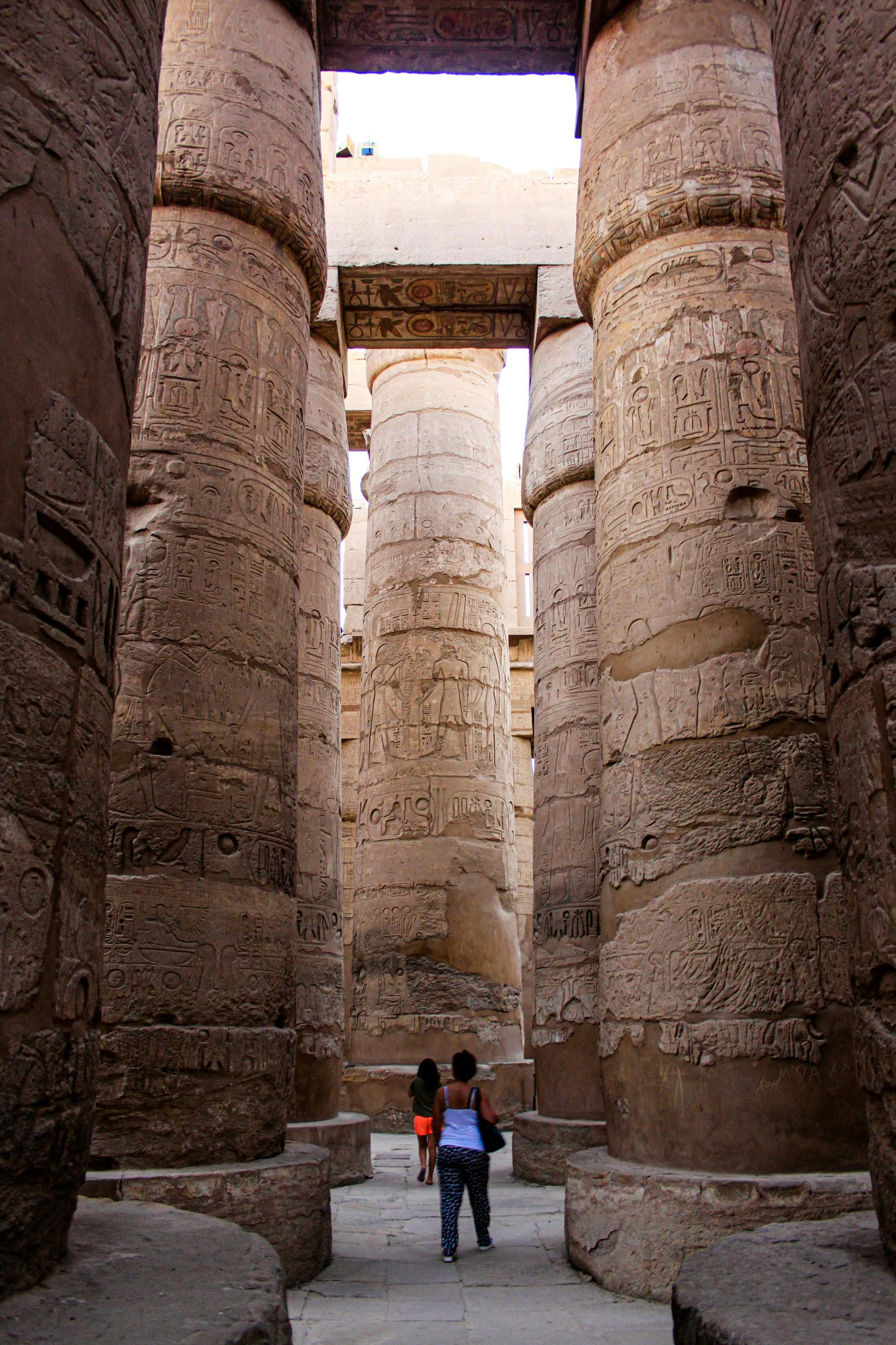 Low-angle view of massive sandstone columns covered in hieroglyphics inside the Great Hypostyle Hall at Karnak Temple, Luxor.