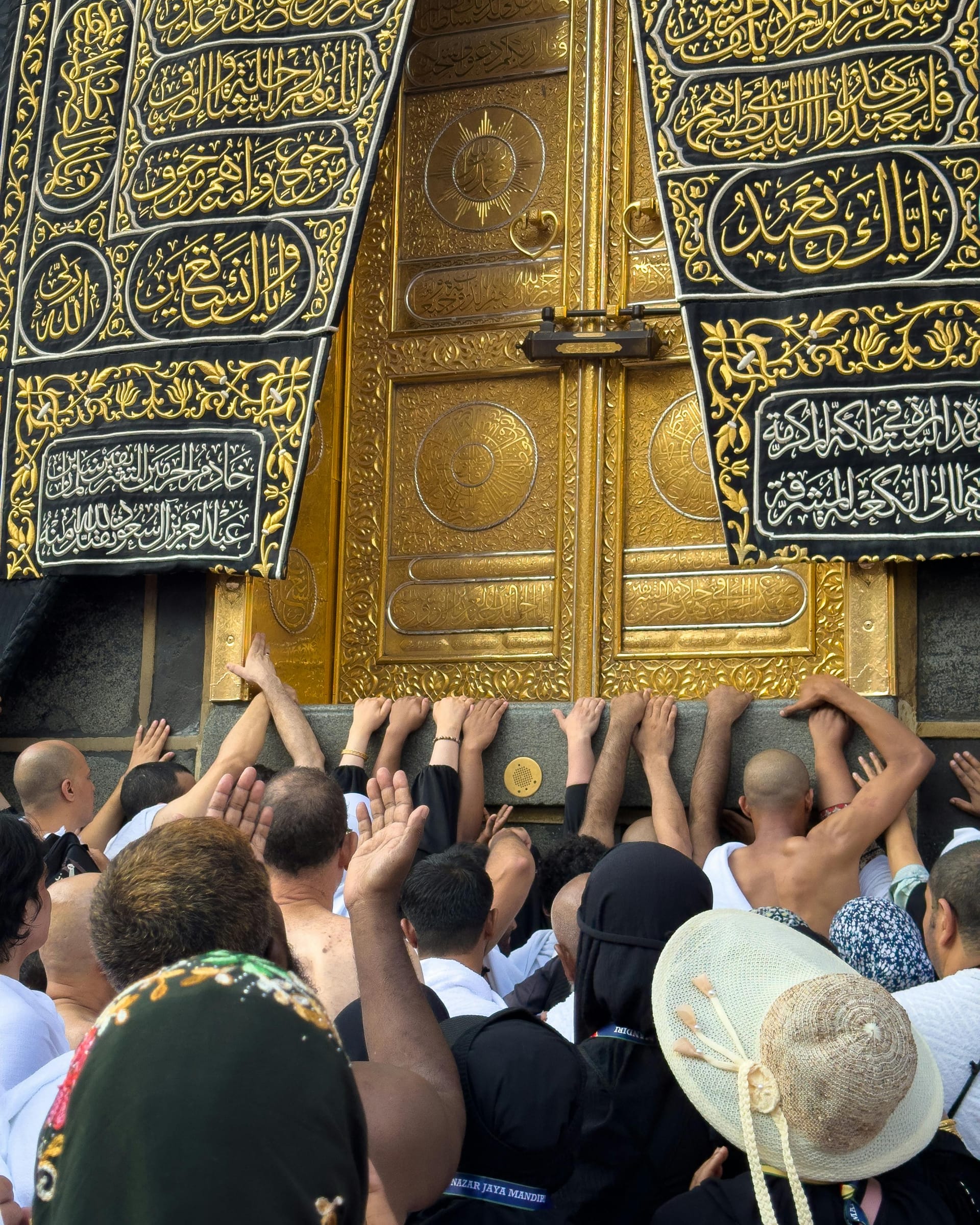 Close-up view of pilgrims' hands reaching up to touch the golden door of the Kaaba.