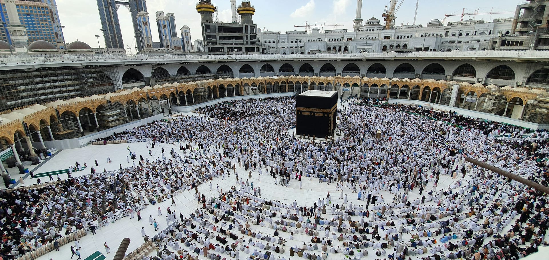 High-angle aerial view of the Kaaba surrounded by thousands of worshippers filling the white courtyard of the Grand Mosque.