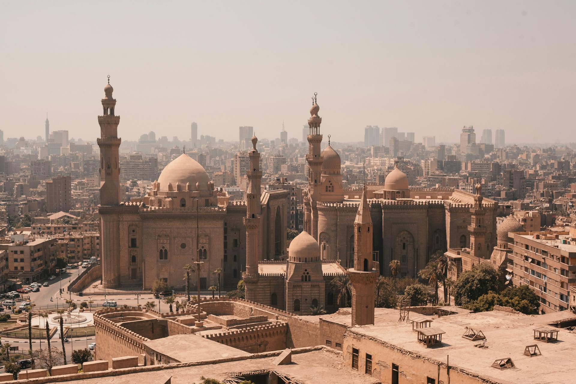 High-angle cityscape view of Islamic Cairo showing the domes and minarets of historic mosques against a hazy sky