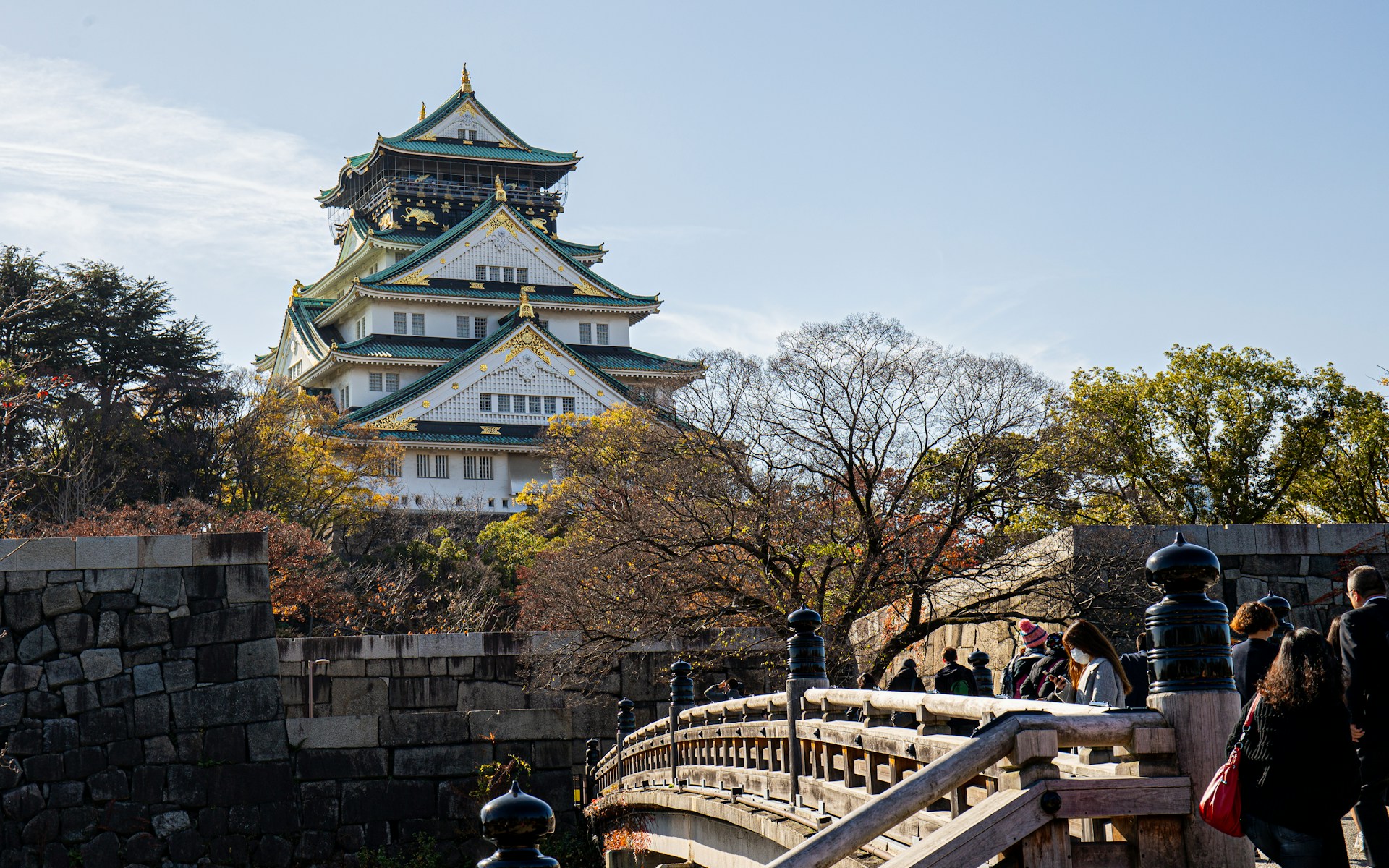 The majestic Osaka Castle with its white walls and green roof, viewed across a moat with a bridge in the foreground.