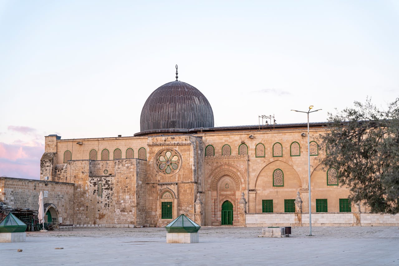 The stone facade and silver dome of the Al-Aqsa Mosque (Qibli Chapel) standing in a large courtyard.